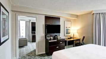 Ein Hotelzimmer mit einem großen Bett, einem Schreibtisch mit Flachbildfernseher, einer Kaffeemaschine und einer Lampe. In der Ecke befindet sich ein Sessel und ein kleiner Tisch.