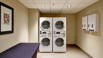 A laundry room with two stacked front-loading washing machines, a table, and a wall-mounted electrical panel.