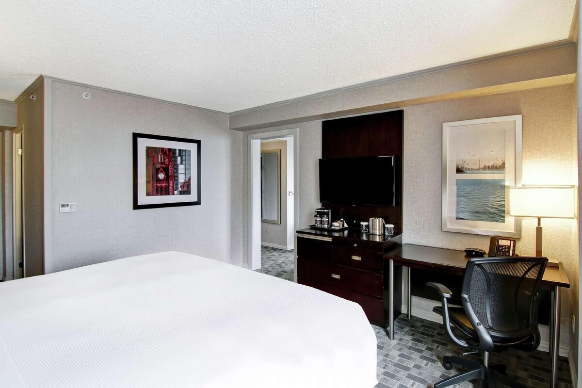 Habitación de hotel con cama, escritorio con silla, televisión y obras de arte en las paredes.