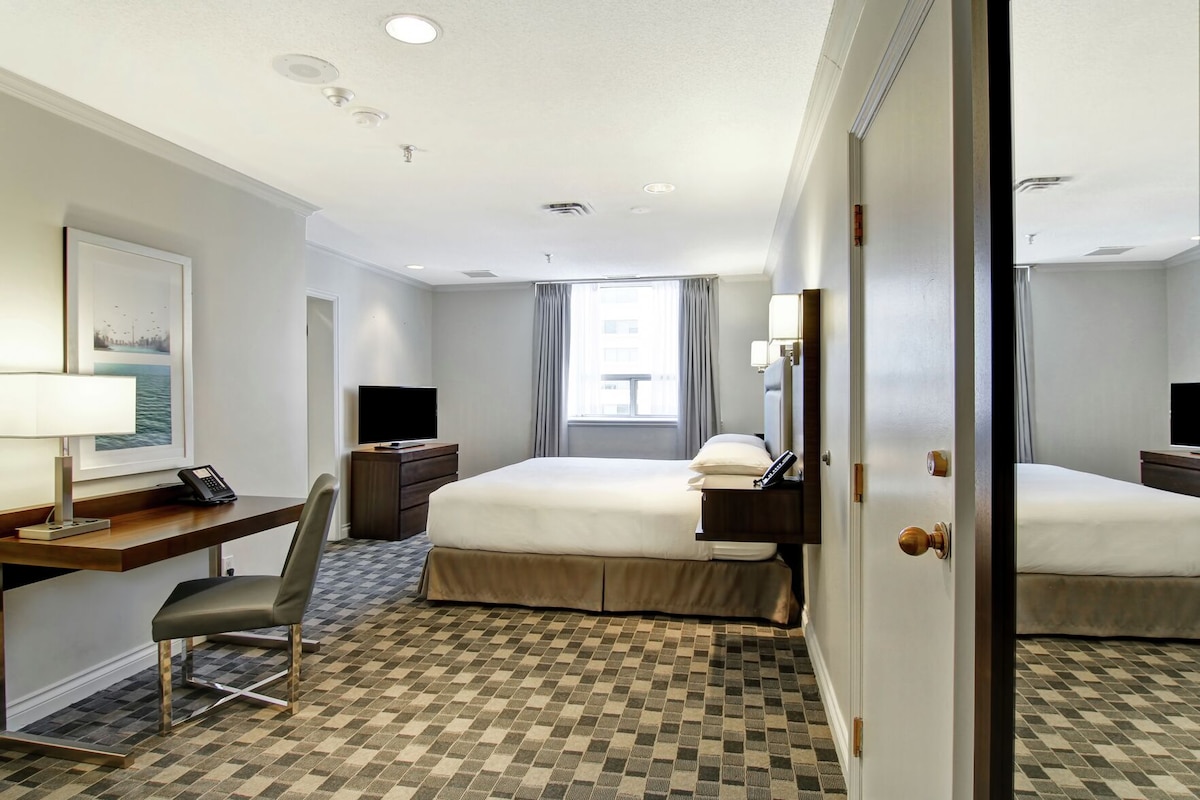 Una habitación de hotel con cama, escritorio, silla y un ventanal grande.