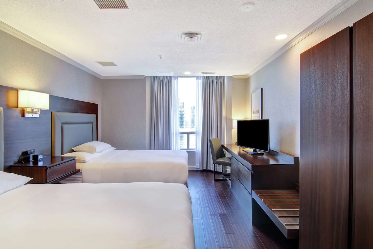 A hotel room with two beds, a desk with a TV, a chair, and a window with curtains.
