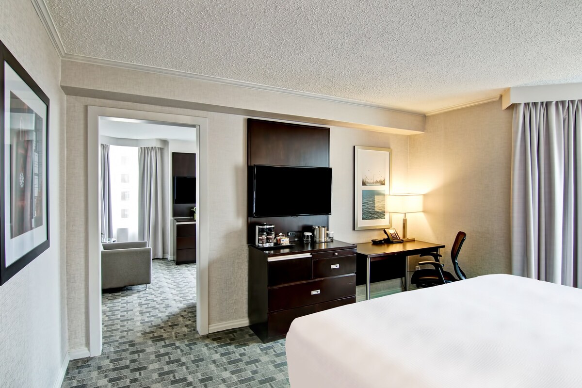 Habitación de hotel con una cama, un escritorio con televisión de pantalla plana, una cafetera, una silla y una lámpara.