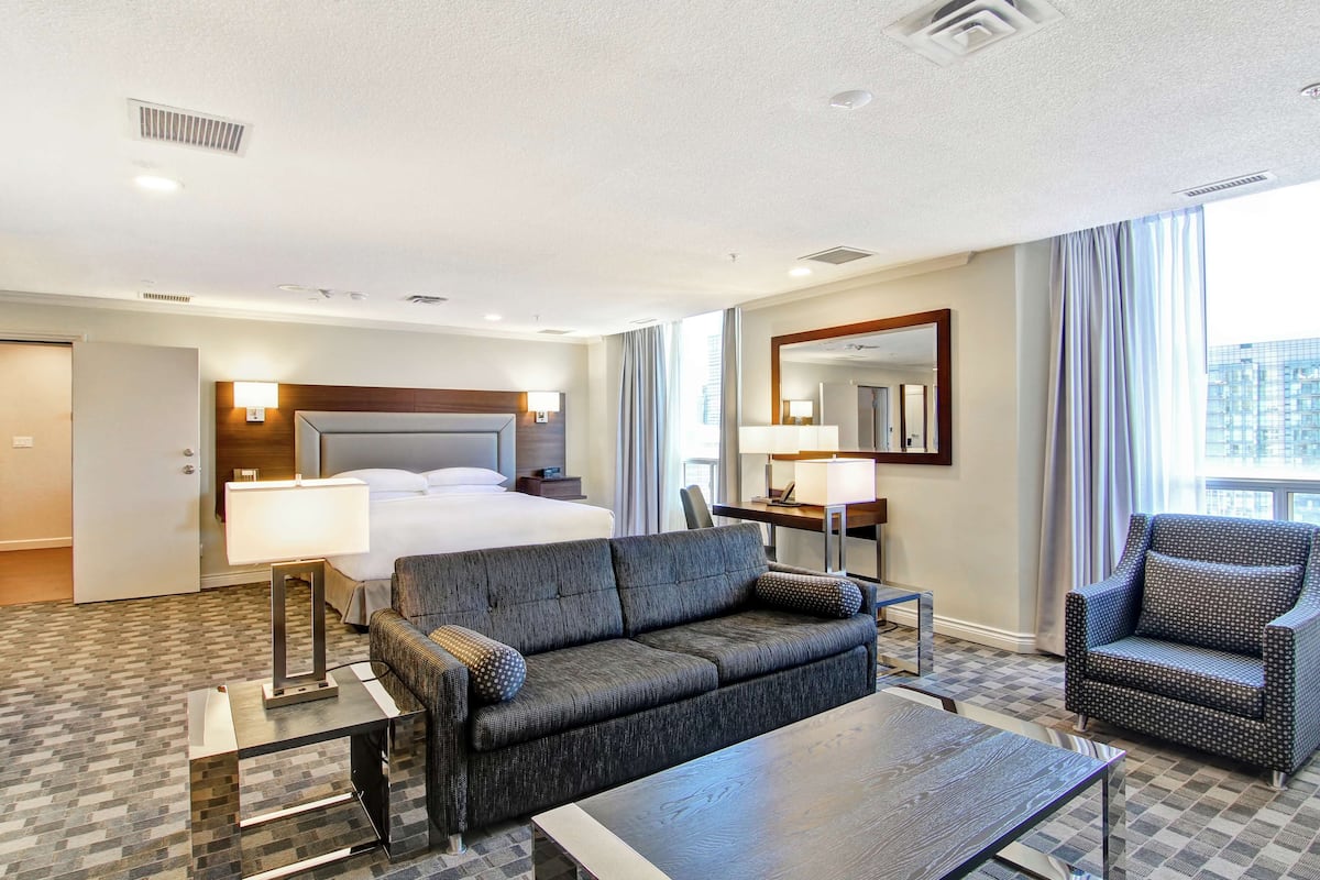 A hotel room with a bed, a sofa, a chair, a desk, and a large window.
