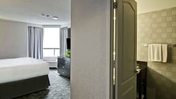 Quarto de hotel com cama, penteadeira, banheiro com porta-toalhas e janela com cortinas.