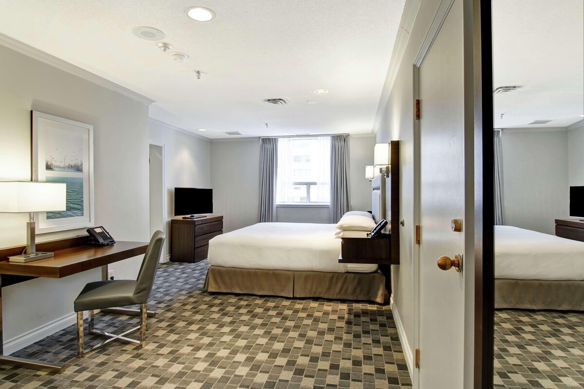 Habitación de hotel con cama, escritorio, silla y vista a la ciudad por la ventana.