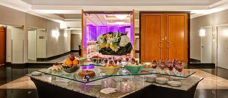 A hotel lobby with a reception desk, a buffet area with various food items, and a large wooden door labeled "MANDARIN B".