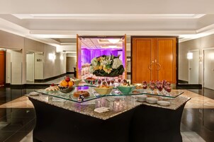 A hotel lobby with a reception desk, a buffet area with various food items, and a large wooden door labeled "MANDARIN B".