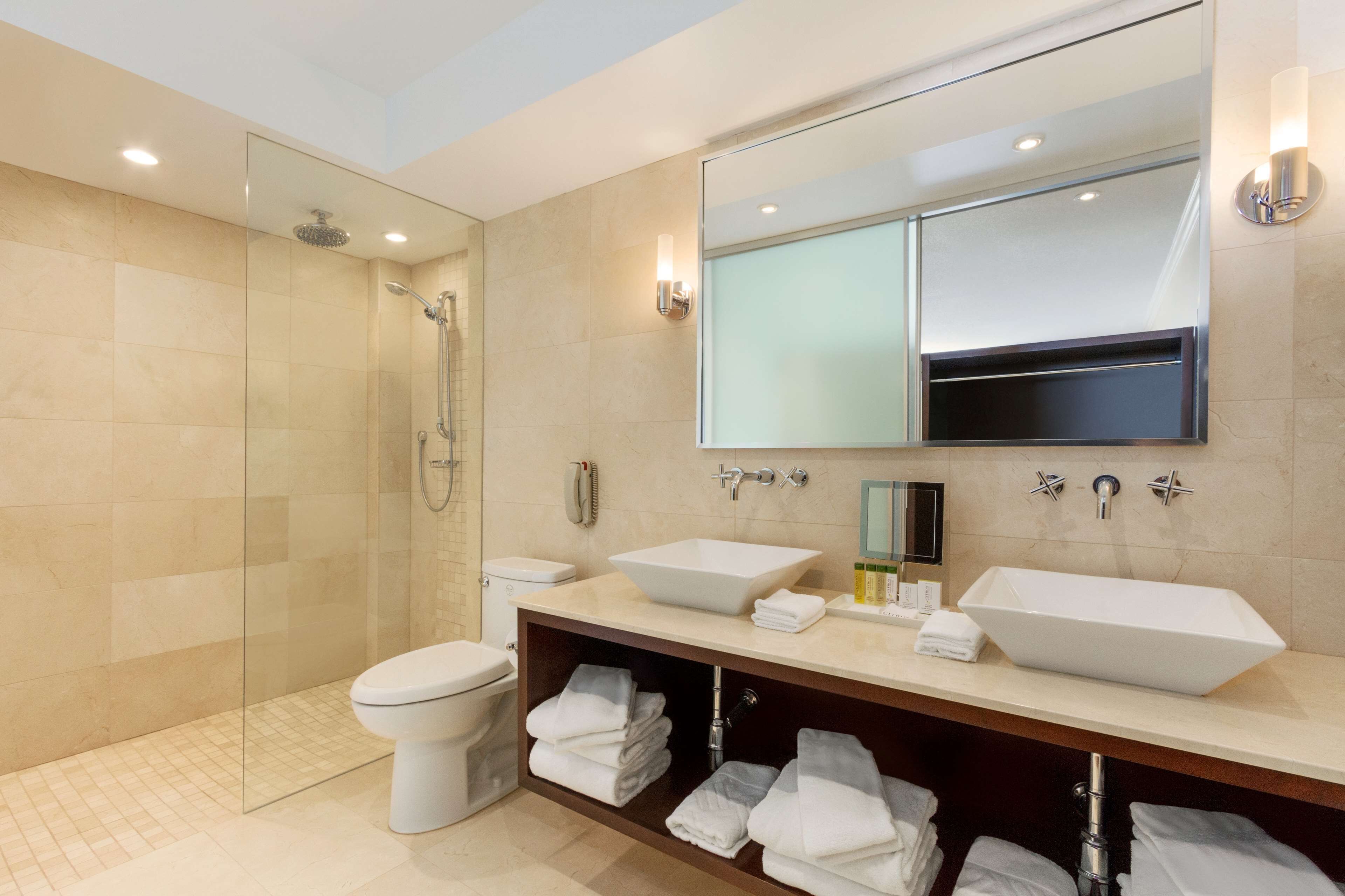 A modern bathroom with a glass-enclosed shower, two sinks, a toilet, and a vanity with towels.