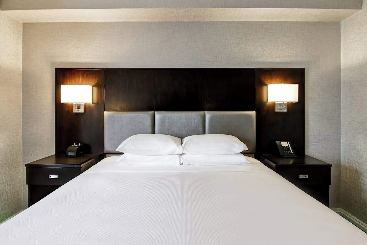 Habitación de hotel con una cama grande, dos mesitas de noche, cabecera con iluminación integrada y teléfono en cada mesita.