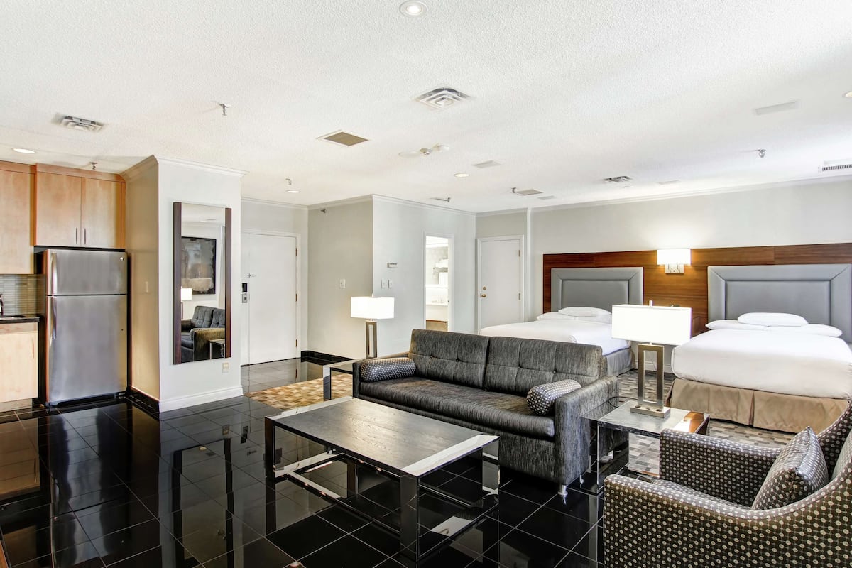 A modern hotel room with a kitchenette, a sofa, a dining table, and a bed with a headboard.