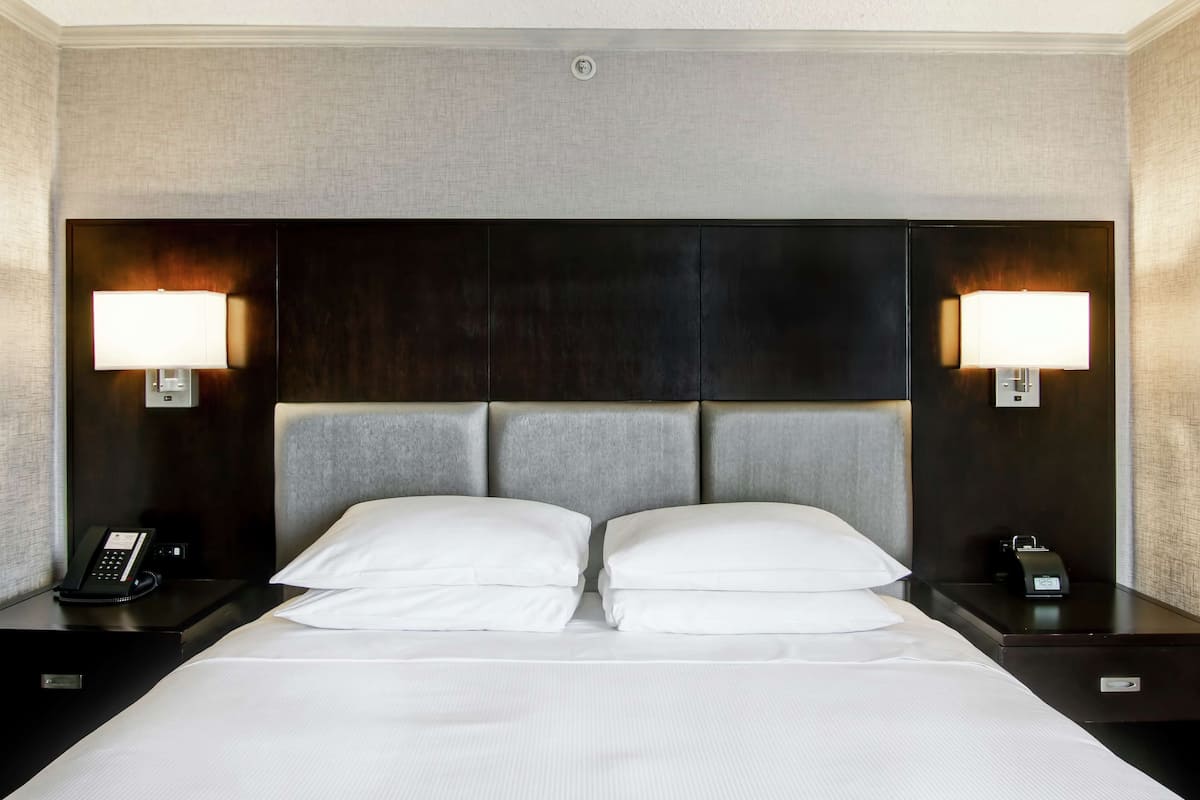 A neatly made bed with white linens, two bedside lamps, and a phone on the nightstand.
