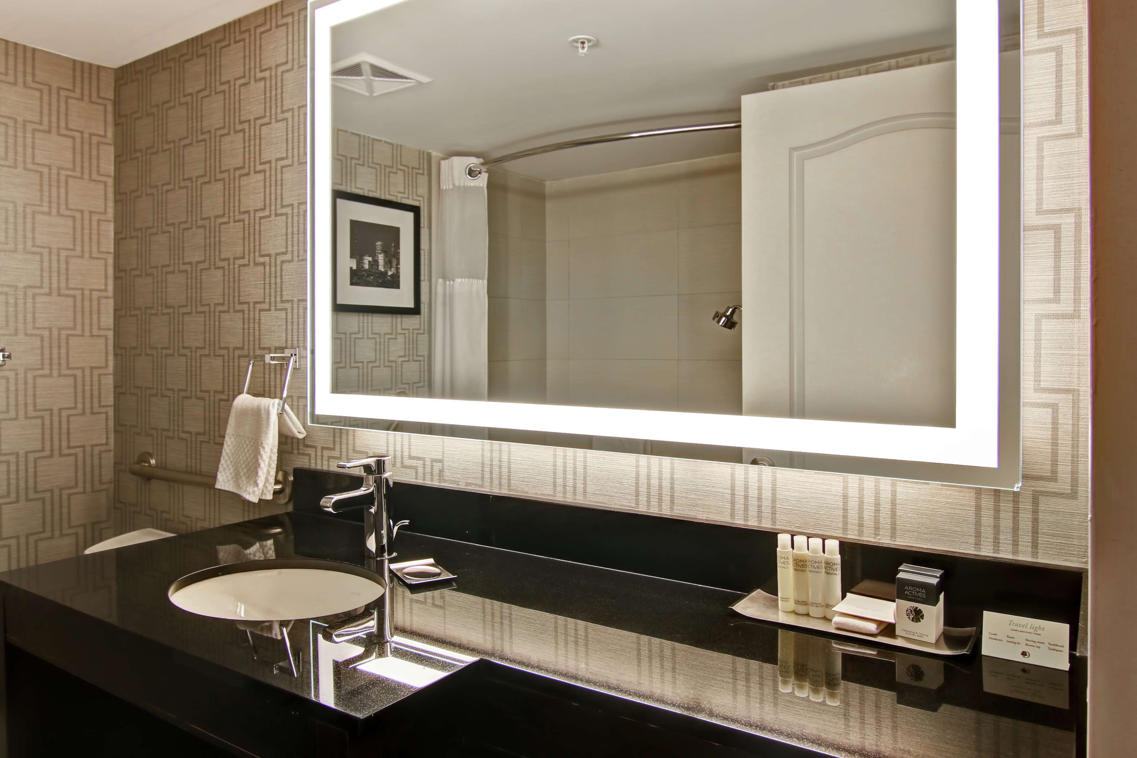 A modern bathroom with a large mirror, a black sink, and a shower visible in the reflection.