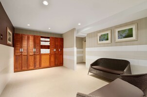 Un baño moderno con un mueble de tocador grande de madera, una silla de mimbre y decoración de pared a rayas.