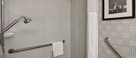 A bathroom with a shower, grab bars, a towel rack, and a framed cityscape picture on the wall.