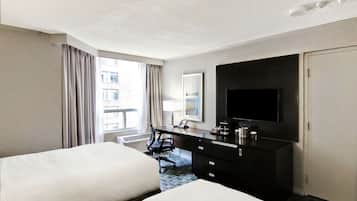 A hotel room with two beds, a desk with a flat-screen TV, a dresser, and a window with curtains.