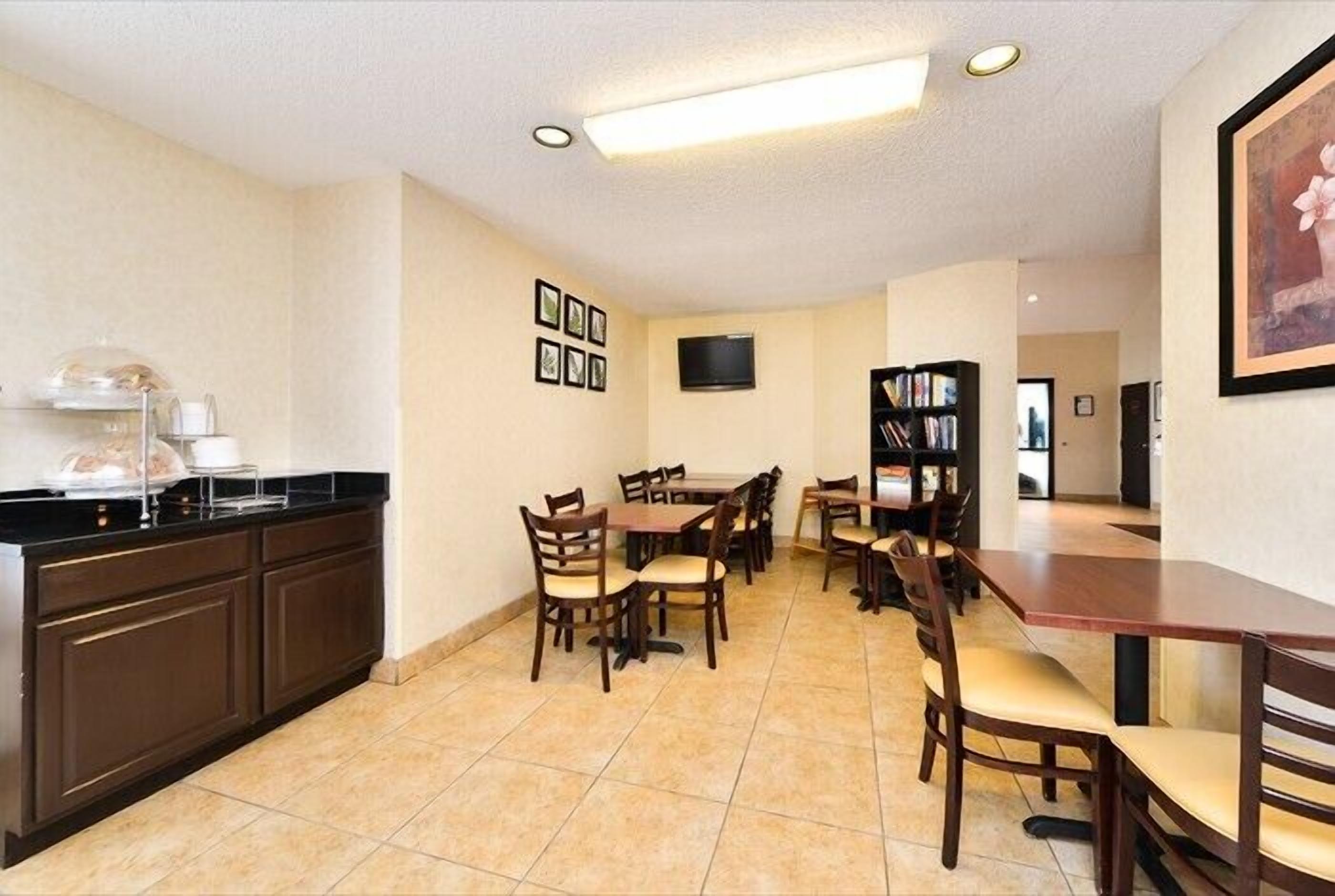A dining area with multiple tables and chairs, a kitchen area with a counter and appliances, and a television mounted on the wall.