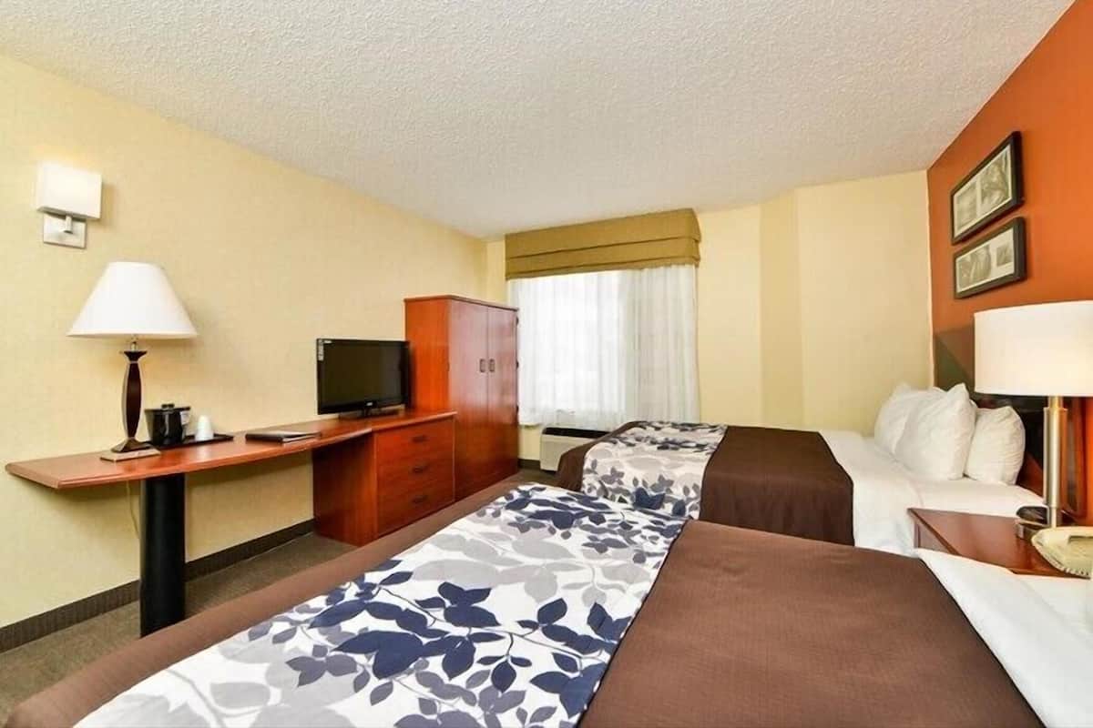 Habitación de hotel con dos camas, un escritorio con televisor, un armario y una ventana con cortinas.