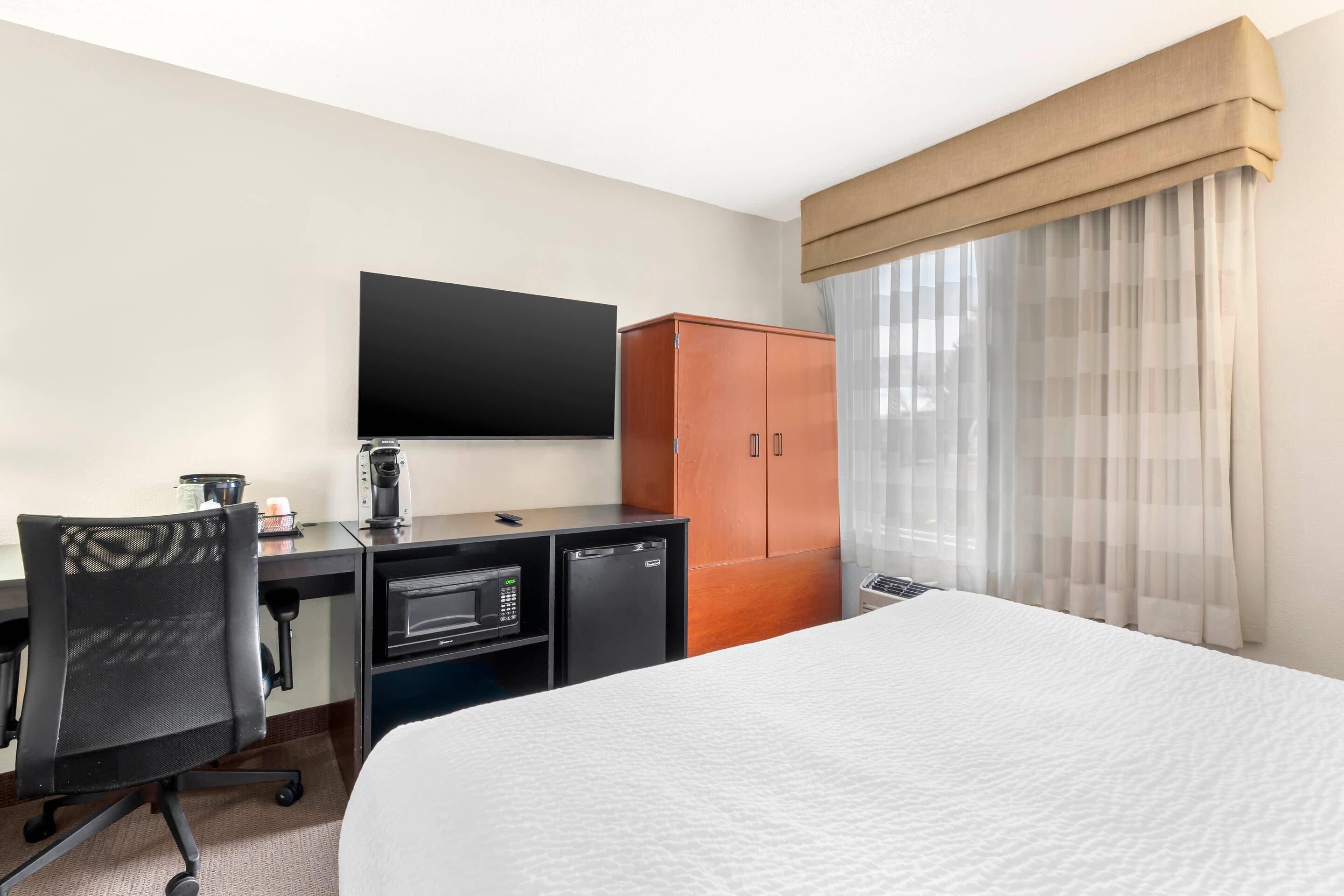A hotel room with a bed, a desk with a computer, a television, a wardrobe, and a microwave.
