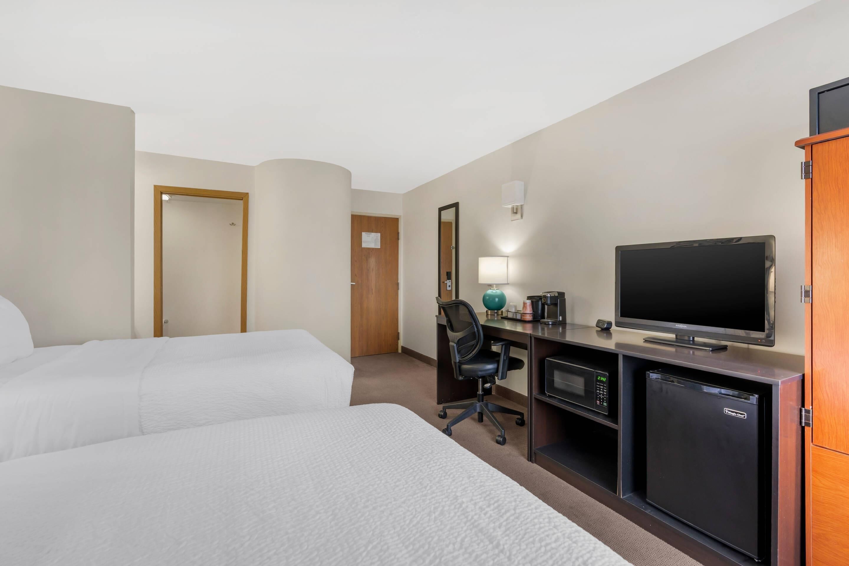 Habitación de hotel con dos camas, un escritorio, televisión, microondas y refrigerador.