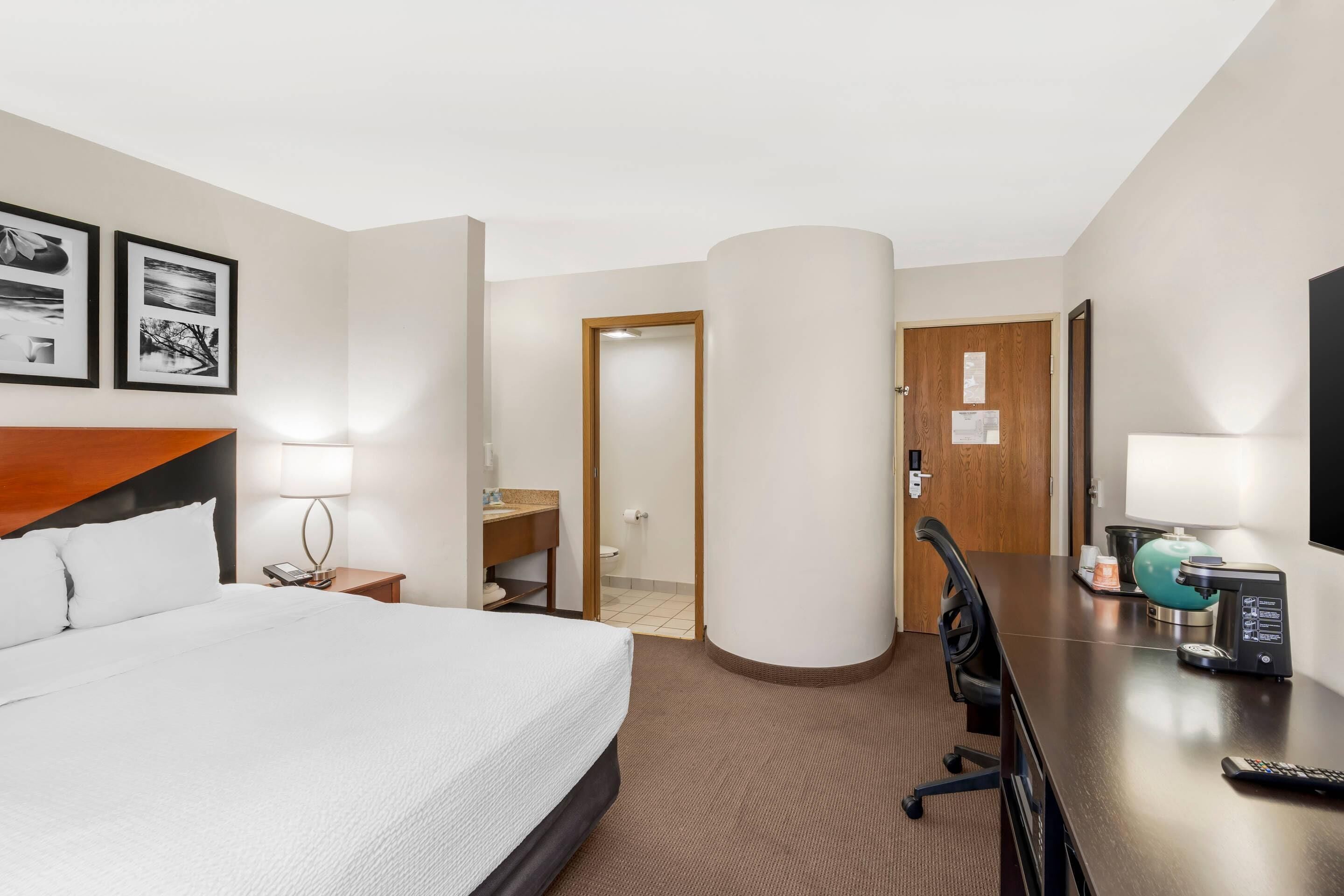 A hotel room with a bed, a desk, a chair, a lamp, and a television.