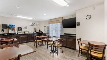 Un comedor de hotel con mesas y sillas de madera, una zona de cocina con electrodomésticos y un reloj en la pared.
