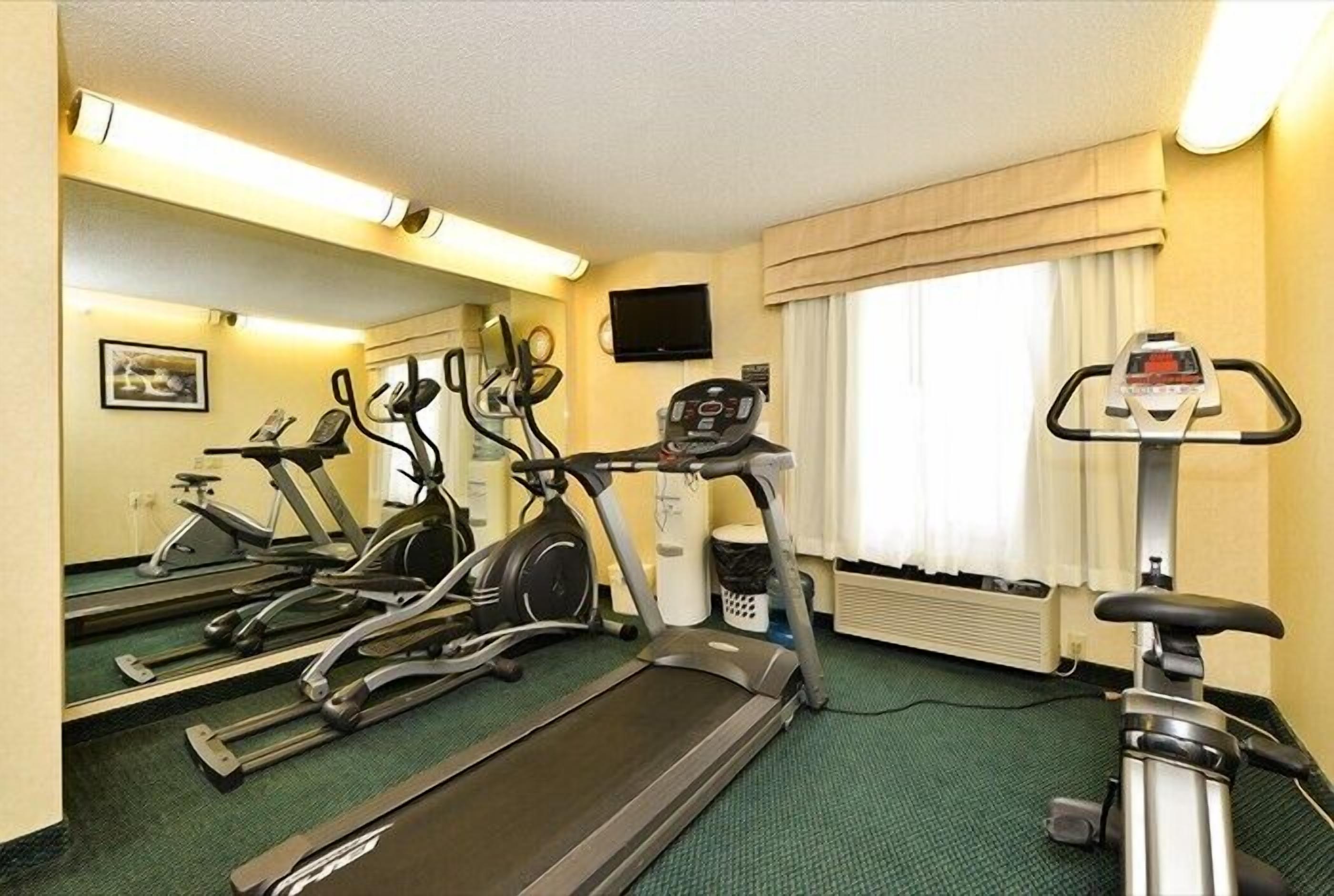 A hotel room with a treadmill, stationary bikes, and a television on the wall.