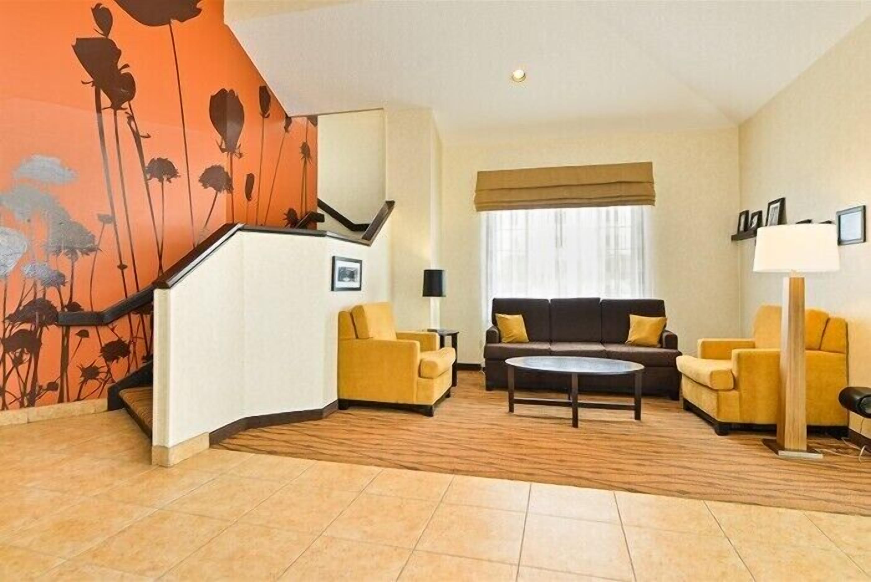 A modern living room with a sofa, armchairs, and a coffee table. There is a staircase with a floral mural on the wall.