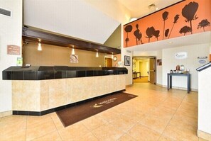 A hotel reception area with a reception desk, a brown welcome mat, and a wall with floral decorations.
