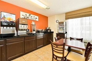 A compact kitchen with a coffee machine, a juice dispenser, and a refrigerator.
