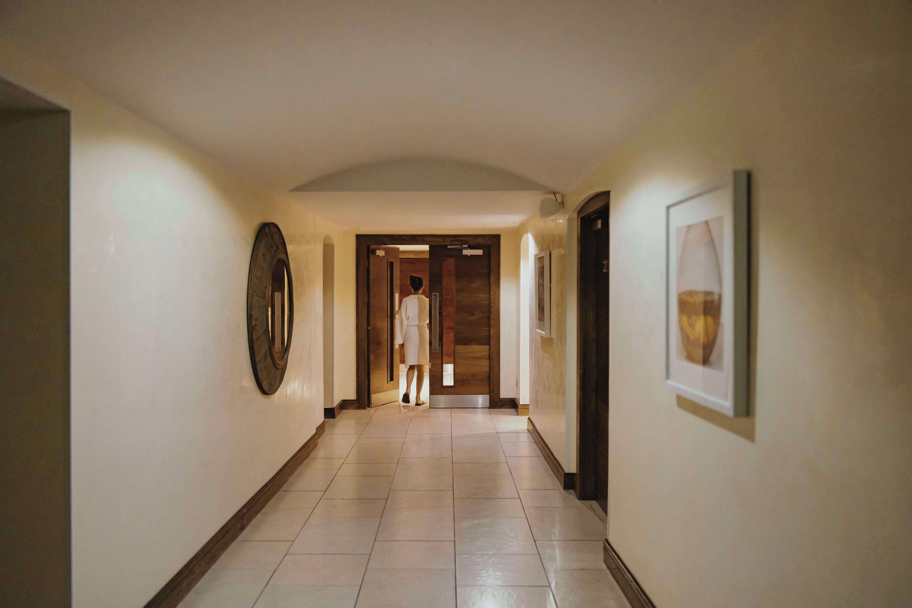 A hallway with a tiled floor, a large mirror on the left, and a framed picture on the right.
