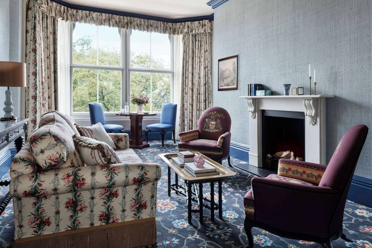 A traditional room with a floral-patterned sofa, a purple armchair, a blue chair, and a fireplace.