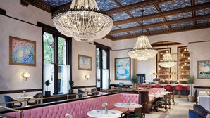 A restaurant with pink booths, round tables, and chandeliers.