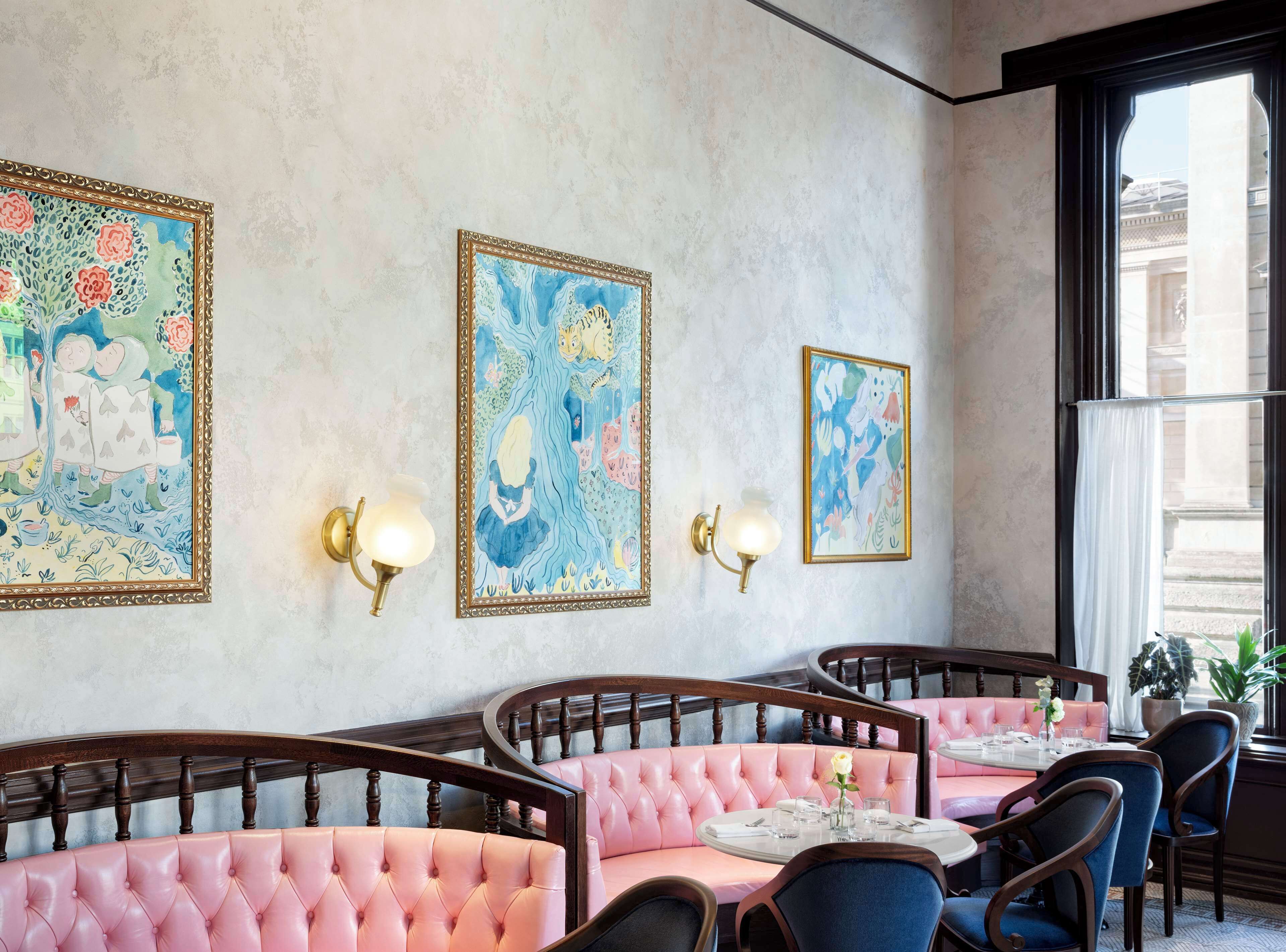 A dining area with pink upholstered booths, a round table, and wall-mounted light fixtures.