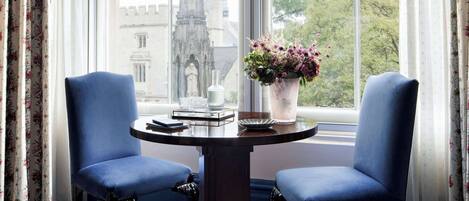 A room with a large window, two blue chairs, a round table with a vase of flowers, and a patterned carpet.