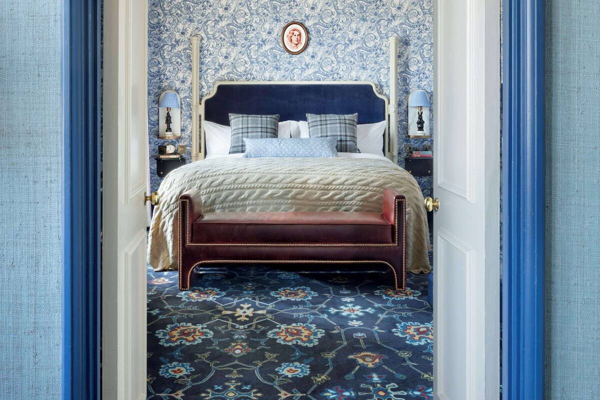 A bedroom with a patterned carpet, a bed with a headboard, and a wall with a decorative pattern.