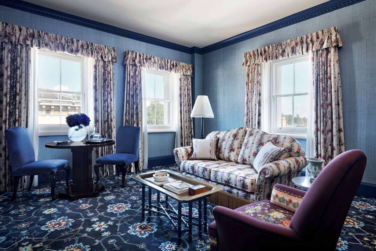 A room with a floral-patterned sofa, two blue armchairs, a small table with a tray, and a lamp.