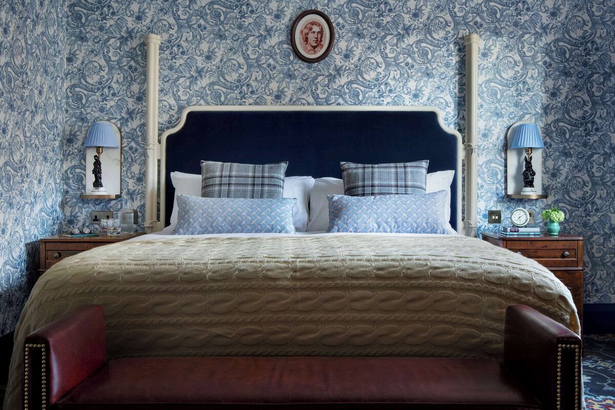 A bedroom with a large bed, two nightstands, a dresser, a mirror, and a wall with a floral pattern.