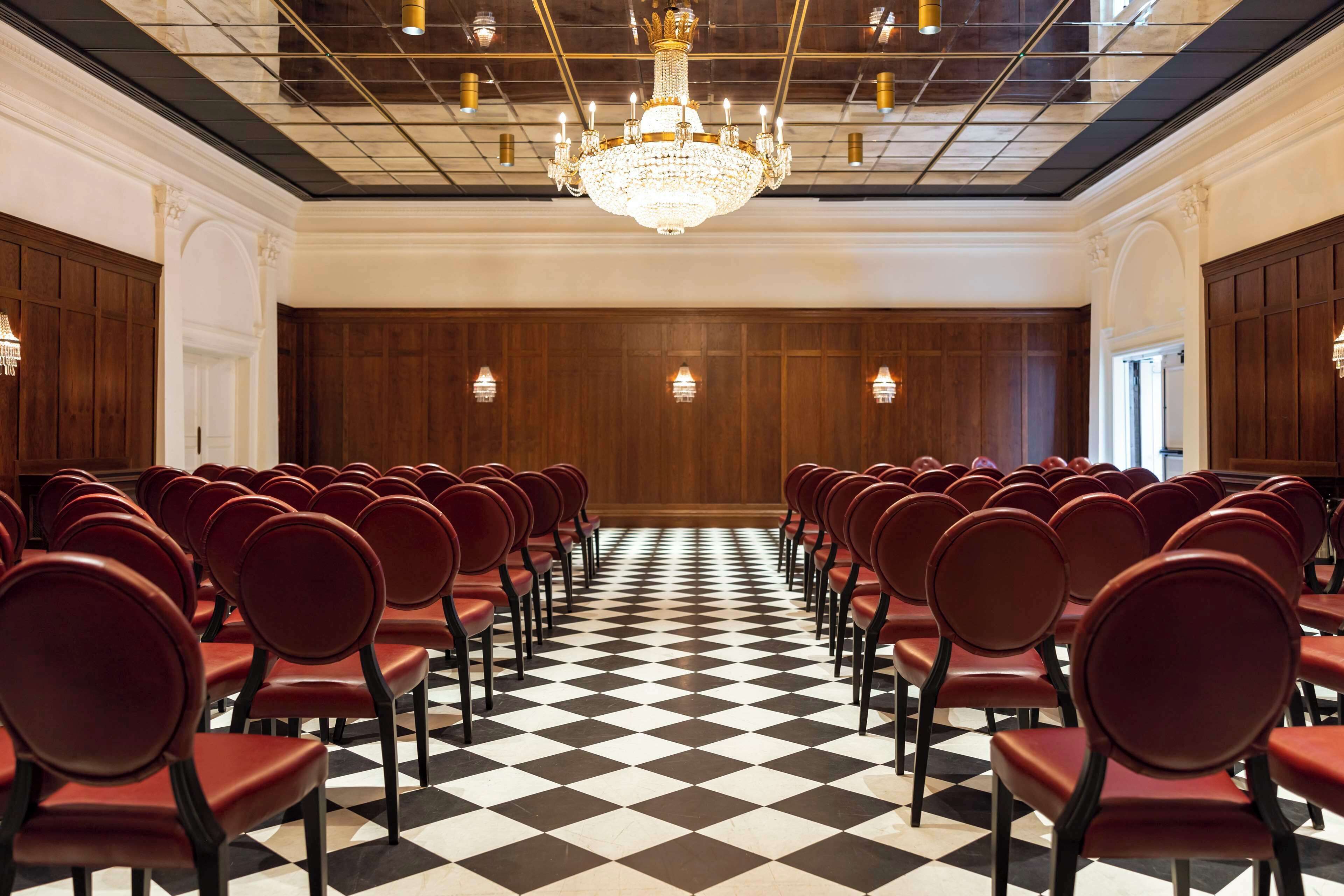 A conference room with rows of red chairs, a black and white checkered floor, and a large chandelier.