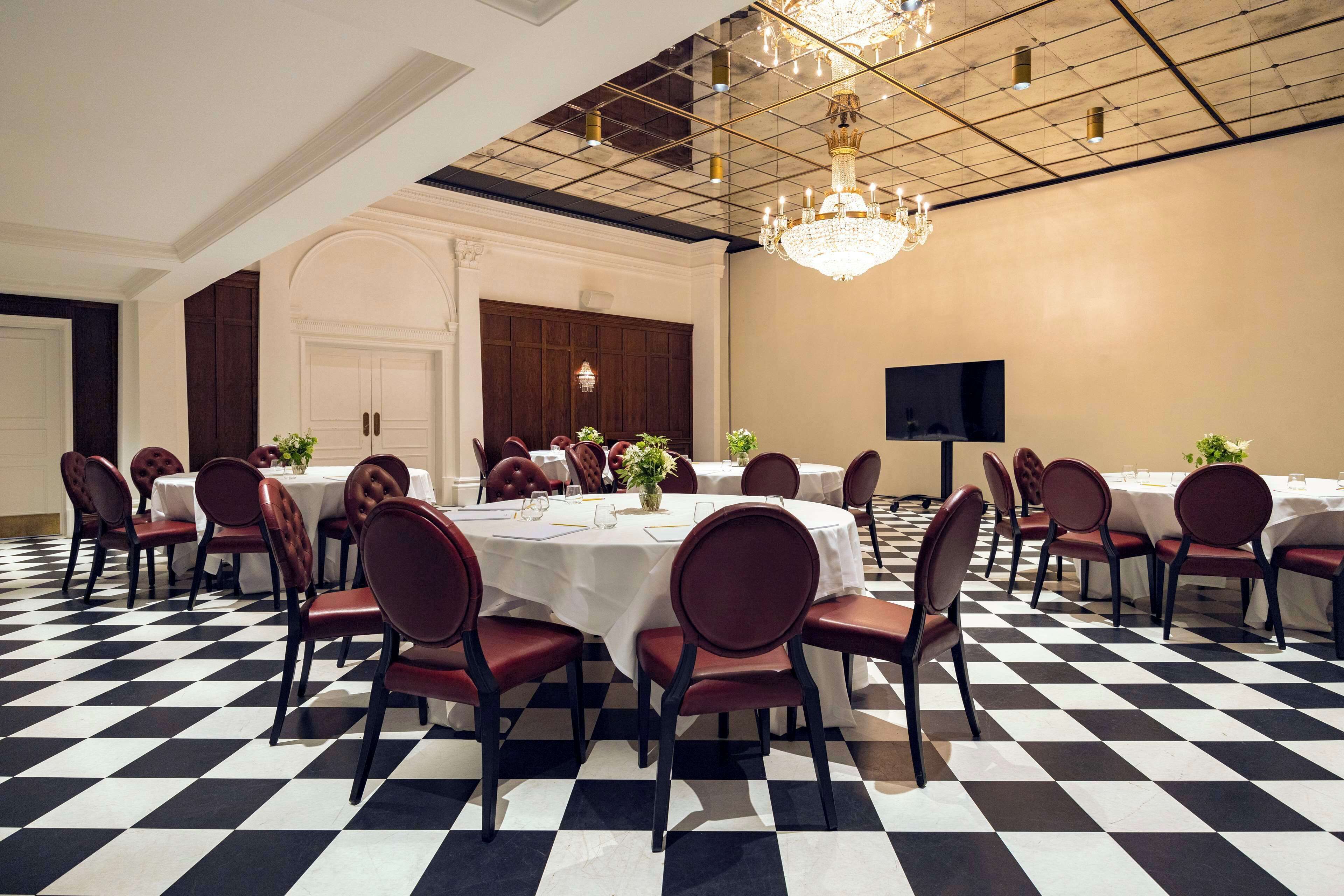 Una sala da pranzo formale con pavimento a scacchi, tavoli rotondi e sedie imbottite rosse.