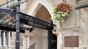 The entrance to The Randolph Hotel with a sign above the door, a green bicycle parked outside, and a flower basket hanging from the wall.