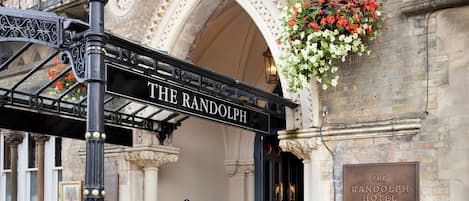 La entrada del Hotel Randolph con un letrero sobre la puerta, una bicicleta verde estacionada afuera y una maceta con flores colgando de la pared.