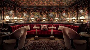 A luxurious room with a red velvet sofa, ornate lamps, and floral wallpaper.