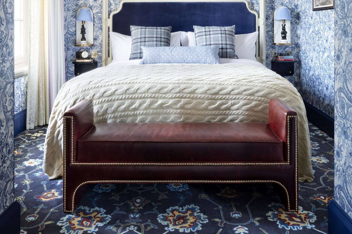 A bedroom with a large bed, a headboard, a nightstand, a lamp, and a patterned carpet.