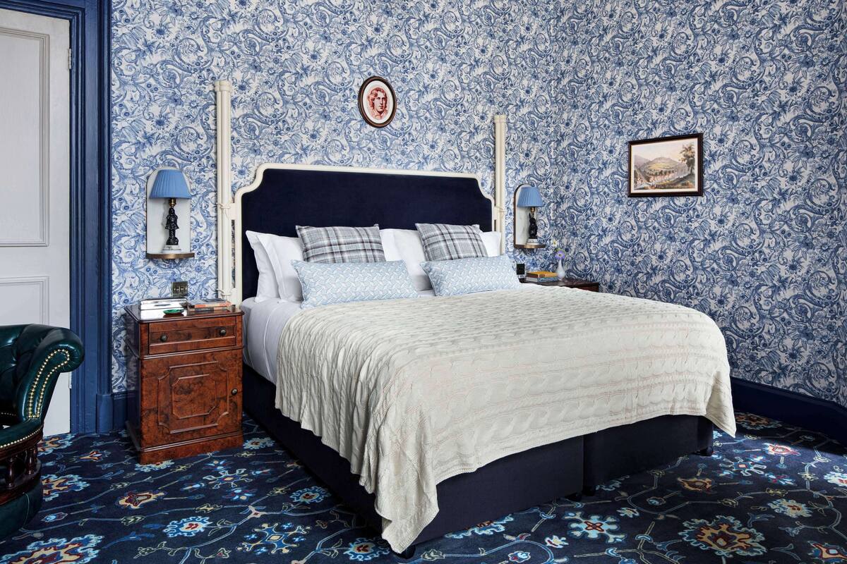 A bedroom with a large bed, two bedside tables, a nightstand, a green armchair, and a patterned carpet.