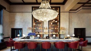 A bar area with a large chandelier, red bar stools, and shelves stocked with bottles.