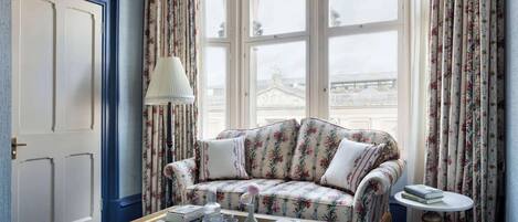 Una habitación con un sofá estampado con motivos florales, una pequeña mesa redonda y una ventana con cortinas florales.