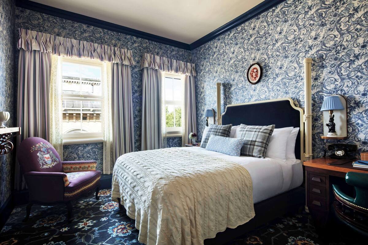 A bedroom with a large bed, a chair, a desk, and a window with curtains.