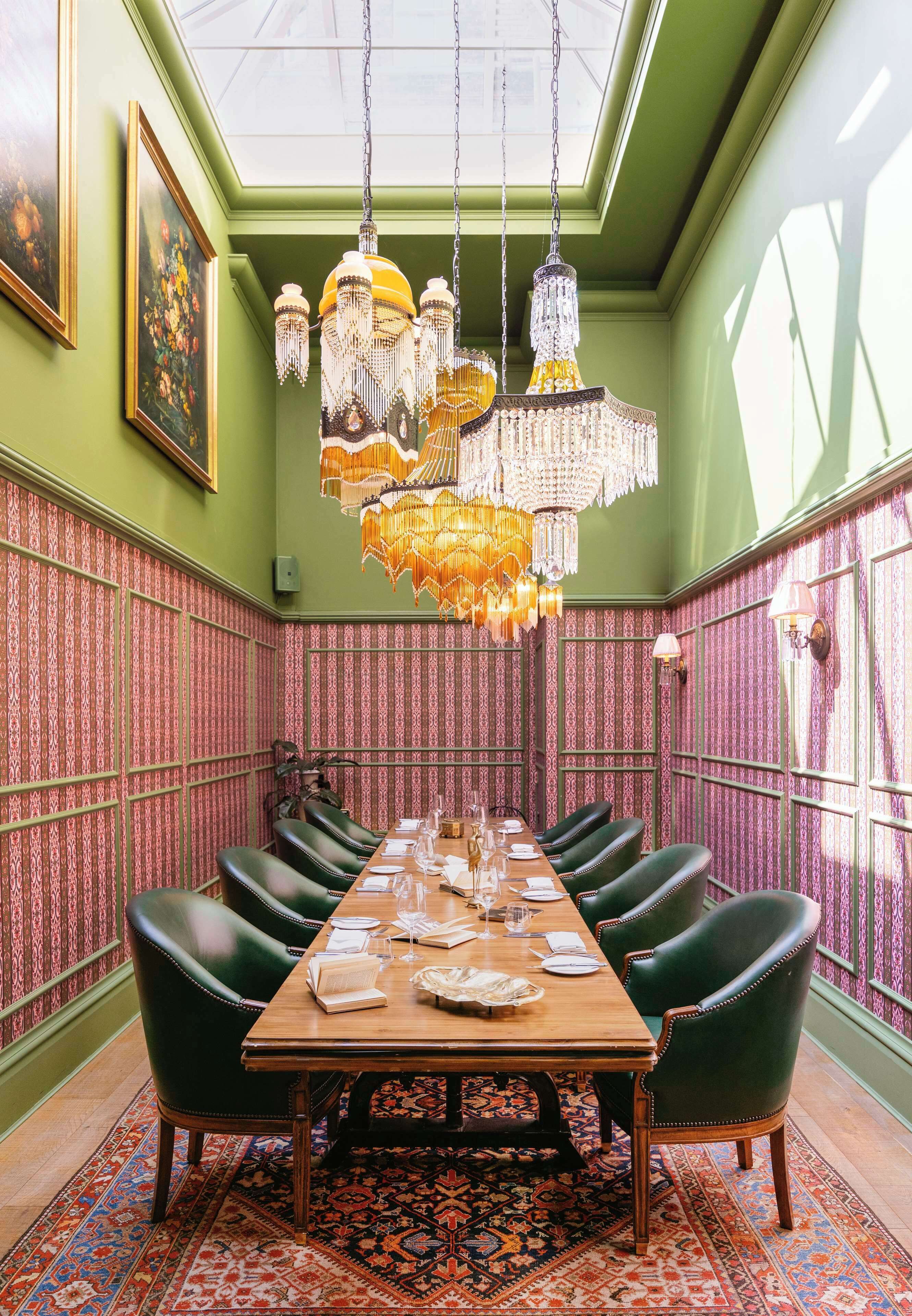 A dining room with a long table, green chairs, and ornate chandeliers.