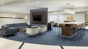 A modern hotel lobby with a sofa, chairs, a coffee bar, and a flat-screen TV. - Courtyard by Marriott Montvale (Montvale)