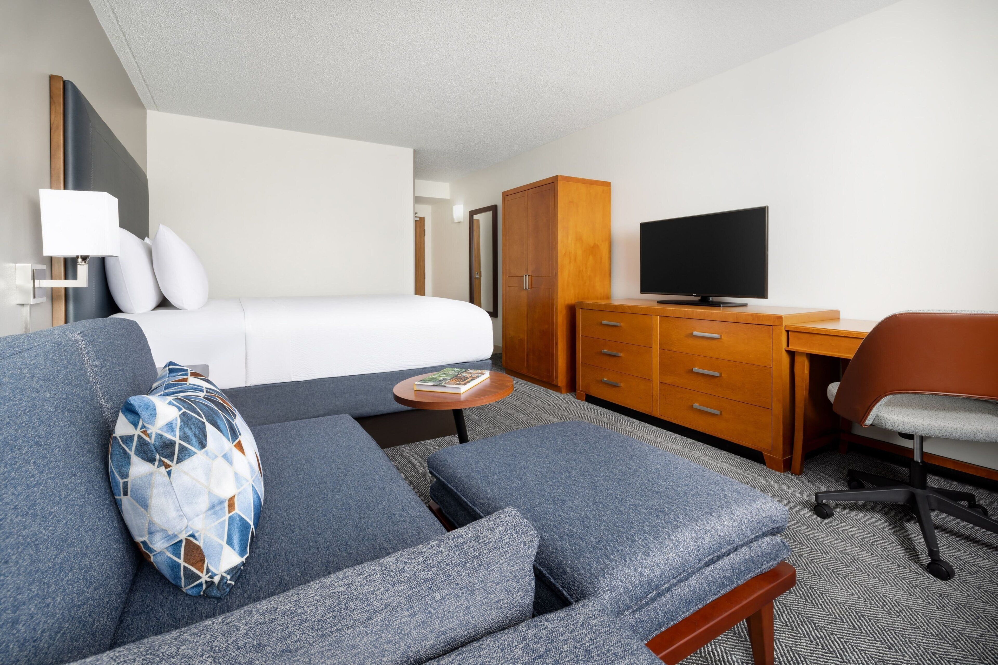 Ein Hotelzimmer mit einem Bett, einem Schlafsofa, einem Schreibtisch, einem Fernseher und einem Kleiderschrank.